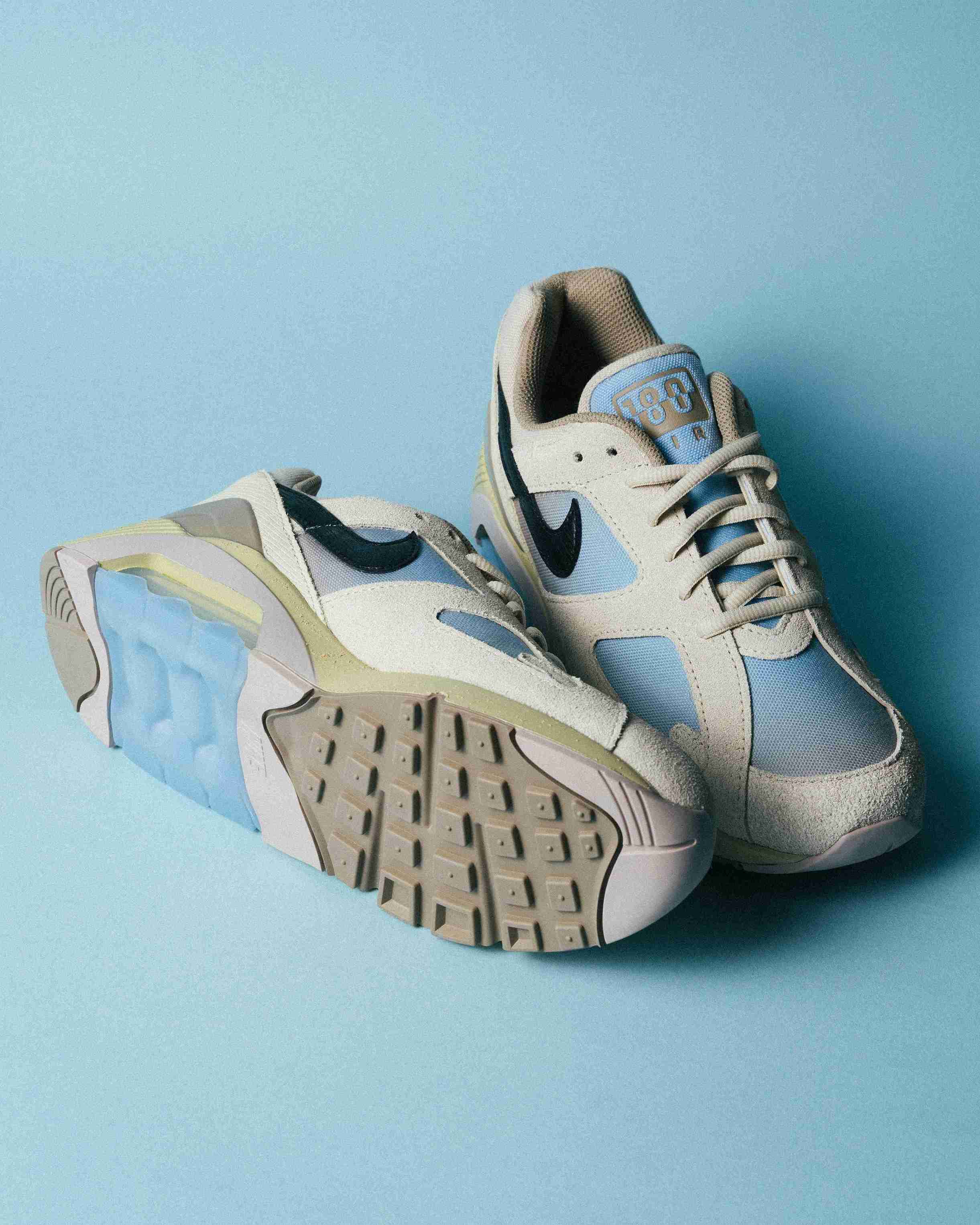 Paire de sneakers beige et bleu clair posée sur un fond bleu, vue de trois quarts avec mise en avant des formes et détails du modèle.
